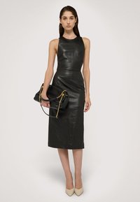 Abito senza maniche in pelle nera con corpetto aderente, design fino al ginocchio; abbinato a una borsa nera con hardware dorato e dettagli in catena.