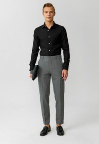 Zwarte overhemd, grijze op maat gemaakte broek, zwarte schoenen, met een zwarte clutch. Soepele stof met een slim fit en strakke lijnen.