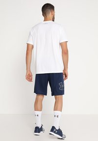 Witte sportshirt met korte mouwen, marineblauwe shorts met logo, witte sokken en donkere schoenen. Eenvoudig ontwerp, lichtgewicht en ademende materialen.