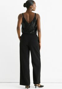 Black sequin top with adjustable straps, paired with high-waisted black wide-leg trousers. Sheer texture and youthful design.