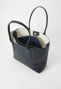 Sac fourre-tout en cuir bleu marine avec finition texturée, deux anses, doublure crème, poche zippée intérieure et fermeture à pression.