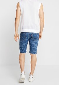 Farkkushortsit, joissa on sinisen sävyinen kamouflagekuvio, yhdistettynä valkoiseen ilmanhihoihin verkkopaitaan. Valkoiset urheilujalkineet täydentävät asun.