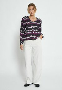 Top nero con motivo a onde viola e bianco; scollo a V, maniche lunghe. Abbinato a pantaloni bianchi a gamba larga e scarpe nere. Tessuto dalla consistenza liscia.