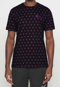 Camiseta de algodón negra con un patrón repetido de pequeñas cruces rojas y azules, con los logotipos de Nike y Barcelona en el pecho. Mangas cortas.