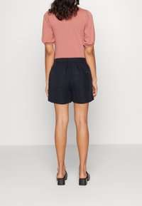 Rust short-sleeve top, paired with dark blue shorts. The shorts feature an elastic waistband and back pockets. Smooth fabric texture.