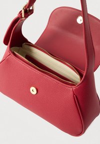 Czerwona skórzana torebka o fakturowanej powierzchni, złotych elementach i wewnętrznej kieszeni na zamek. Projekt jest kompaktowy, o miękkim kształcie.