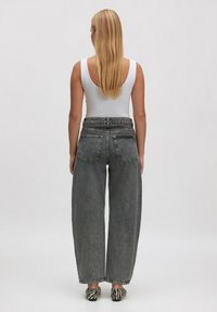 Grijze high-waisted wijde jeans met een textuurafwerking, gecombineerd met een witte tanktop, weergegeven vanuit de achterkant. Zwarte en witte gestreepte schoenen zichtbaar.