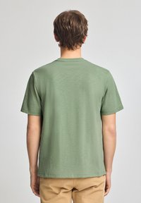 Grön t-shirt med kort ärm, tillverkad av mjuk tyg; har rundad halsringning, rak fåll och avslappnad passform.