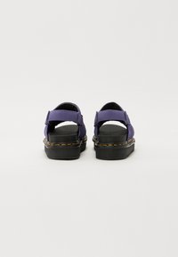 Lilla sandaler med justerbare stropper, polstret såle og svart gummisåle med gul søm. Åpen bakdesign for ventilasjon.