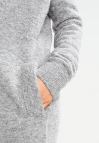 Gray sweater made of soft, textured fabric featuring long sleeves, a relaxed fit, and side pockets. The material appears warm and cozy.