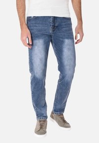 Jeans in denim azzurro chiaro con lavaggio sbiadito, taglio dritto, cinque tasche e cuciture a contrasto, abbinati a sneakers grigie.