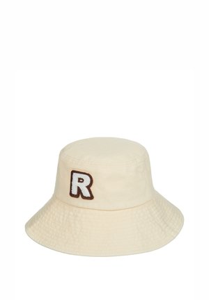 Chapeau seau de couleur crème en coton, arborant une lettre "R" brodée en marron à l'avant et une finition en tissu texturé.