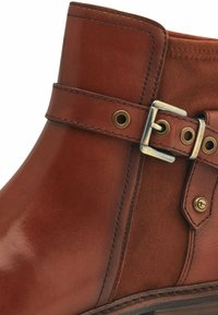 Bottine en cuir marron avec une finition lisse, un panneau en daim, des éléments en métal pour la boucle et des accents dorés sur la sangle et le côté.