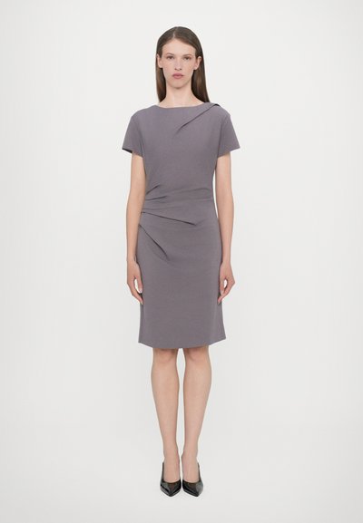 Kurzärmliges, tailliertes graues Kleid mit Raffung an der Taille. Glatte Textur und knielange Schnittform, kombiniert mit schwarzen High-Heels.