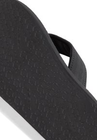 Black flip-flop featuring a textured rubber sole and a fabric strap. The sole displays a honeycomb pattern for traction.