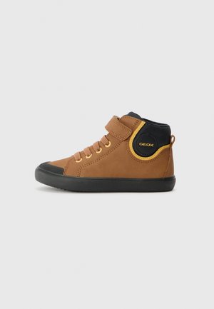 Baskets montantes marron avec des accents noirs et jaunes, semelle noire, lacets et sangle Velcro latérale.