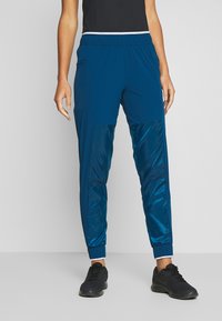 Blaue Sporthosen mit einer Mischung aus matten und glänzenden Texturen, elastischem Bund und Bündchen. Verfügt über Seitentaschen für zusätzliche Funktionalität.