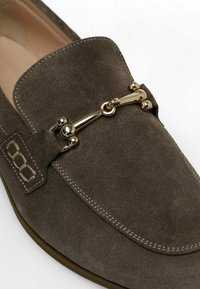 Mocassini in suede grigio scuro con punta arrotondata, caratterizzati da un accento in metallo dorato e una cucitura decorativa sulla tomaia.