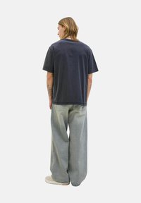 Donker marineblauwe oversized katoen t-shirt met korte mouwen, gecombineerd met lichtgrijze wijde spijkerbroeken en off-white sneakers.