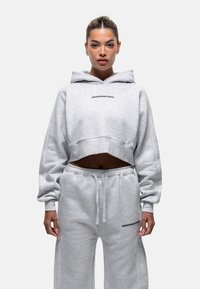 Hoodie grigio corto e pantaloni abbinati con una texture liscia. Il hoodie presenta un cordino e un logo nero sia sulla parte anteriore che sui pantaloni.