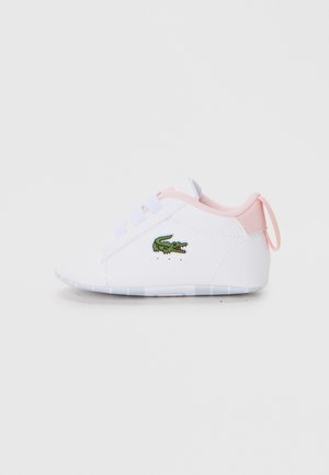White sneaker with pink accents, textured rubber sole, lace-up design, and green embroidered crocodile logo on the side.