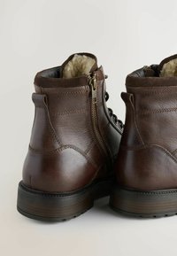 Bruine leren enkelboots met een gestructureerd oppervlak, metalen zijrits en een zachte binnenvoering. Robuuste zool met een lichte hakverhoging.