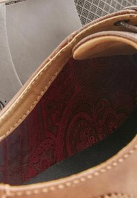 Unutrašnjost kožne cipele s bordo paisley uzorkom, svijetlom šavovima i glatkom teksturom na kontrastnoj crnoj podlozi.