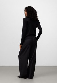 Zwarte gebreide trui met lange mouwen, gecombineerd met zwarte broek met wijde pijpen. De gestructureerde stof heeft een subtiele glans en biedt een gestroomlijnde siluet.