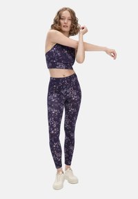 Bloemen sportset bestaande uit een donkerpaarse crop top en bijpassende leggings, beide met een zachte textuur en ingewikkelde bloemmotieven.