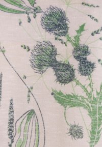 Tissu floral présentant des motifs de chardons verts et de feuilles sur un fond rose clair. Surface texturée avec des détails et des lignes complexes.