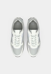 Αθλητικά παπούτσια σε λευκό με γκρι πλέγμα στα πάνελ, σχέδιο με κορδόνια, λογότυπο στη γλώσσα και στο πλάι, επίπεδη σόλα από καουτσούκ και στρογγυλεμένο σχήμα μύτης.