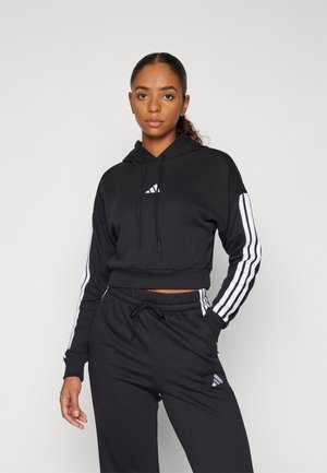 Zwarte cropped hoodie met een trekkoord, wit adidas-logo op de borst en witte drie-strepen accenten op de mouwen, gecombineerd met bijpassende zwarte sweatpants.
