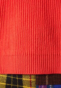 Tissu en tricot côtelé rouge en haut, associé à une section écossaise noire, jaune et rouge en dessous, présentant une texture douce.