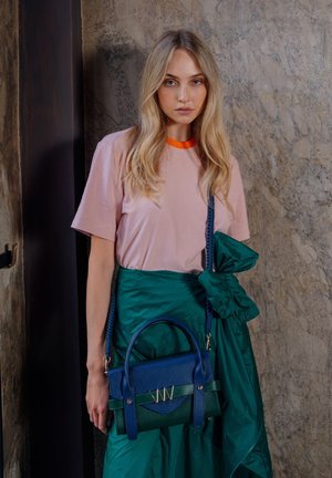 Rosa T-Shirt mit orangenem Halsausschnitt, kombiniert mit einem grünen Rock. Eine blaue Handtasche hat ein strukturiertes Design, kontrastierendes Zubehör und Akzente.