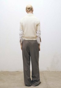 Jasnobeżowy krótki sweter z dzianiny z krótkim rękawem na białej koszuli z długim rękawem, w połączeniu z luźnymi, jasnobrązowymi, dopasowanymi spodniami.