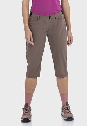 Braune Shorts in Kniehöhe aus leichtem Stoff mit seitlichen Taschen, Knopfverschluss und Gürtelschlaufen. Kombiniert mit pinken Socken und Schuhen.