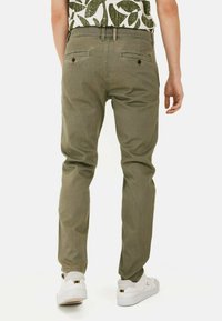 Oliwkowe chinosy o slim fit, z dwoma tylnymi kieszeniami i średnim stanem. Połączone z białymi trampkami.