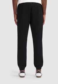 Zwarte sweatpants van zachte stof, met een elastische tailleband en boorden. Gemaakt met witte en zwarte sneakers. Zichtbare achterkant.
