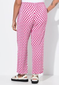 Pantaloni a scacchi rosa e bianchi con un design leggermente svasato, vita elasticizzata e orlo sfrangiato, abbinati a sandali chiari.
