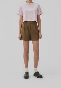 Lyserød cropped T-shirt, olivengrøn plisseret shorts med talje og knap. Sorte slip-on sko og cremegule sokker fuldender outfittet.