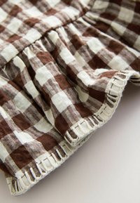Tissu à carreaux marron et blanc avec texture froncée et couture blanche en boucle le long du bord sur une surface claire.