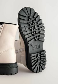 Stivale alla caviglia in pelle beige chiaro con suola in gomma nera, caratterizzato da un motivo di battistrada testurizzato e una cerniera laterale per la chiusura.