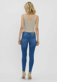 Top de tirantes beige con textura acanalada y espalda en V, combinado con jeans ajustados de mezclilla azul y tacones altos beige. El conjunto presenta un diseño y textura clásicos.