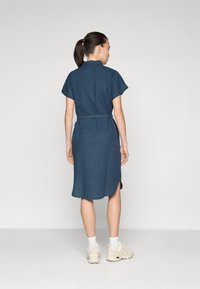 Φόρεμα τζιν με κοντά μανίκια, ζωνάκι στη μέση και πλαϊνές σχισμές. Διαθέτει γιακά και μήκος έως το γόνατο, σε σκούρο μπλε χρώμα.