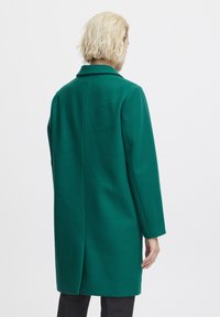 Green wool coat with a straight cut, notched collar, and long sleeves. Features a back vent for movement and a smooth texture.