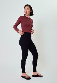 Suurte varrukatega burgundia ülikond, millel on logo, koos kõrge vöökohaga mustade retuusidega. Mudel kannab musti sandaale. Sile kangas ja figuuri jälgiv disain.