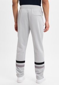 Hellgraue Sporthose mit elastischem Bund, tailliertem Design und schwarzen sowie grauen Akzentstreifen an den Bündchen. Eine einzelne Gesäßtasche.