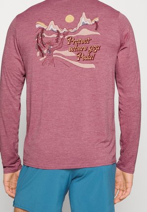 Langärmeliges, bordeauxfarbenes Shirt mit Berg- und Baum-Motiv, Sonne und dem Text „Schütze, wo du trittst“ am oberen Rücken.