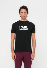 Černé bavlněné tričko s výrazným bílým logem "KARL LAGERFELD". Klasický design s kulatým výstřihem a krátkými rukávy, hladká textura.
