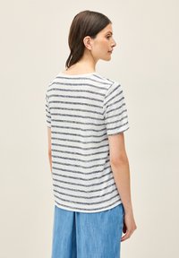 Vit t-shirt med marinblå horisontella ränder, rund halsringning och korta ärmar. Mjuk textur med avslappnad passform. Matchas med ljusblå byxor.